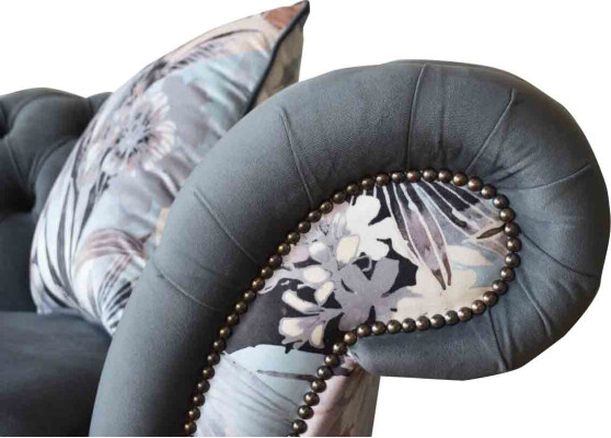 Un llamativo sofá de tres plazas en diseño Chesterfield con delicada decoración de flores grises.