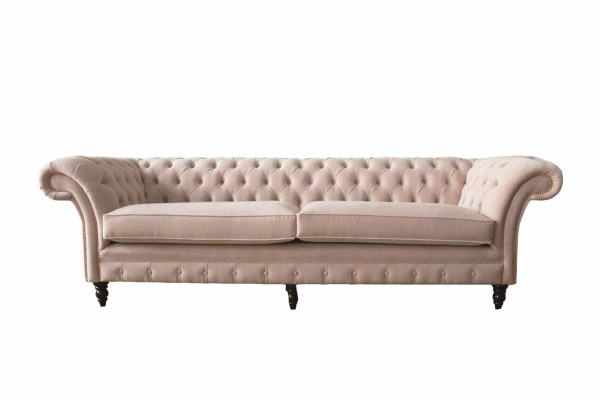 Un lujoso sofá de cuatro plazas de color rosa en diseño Chesterfield, que incluye cojines de asiento.