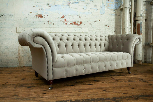 Estiloso sofá Chesterfield de tres plazas de color gris claro para salón de lujo.
