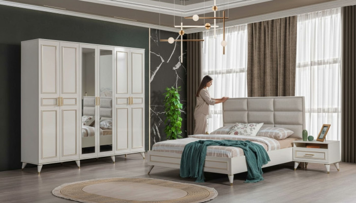 Muebles de dormitorio blancos de madera con armario de vidrio y cama doble de tela con mesitas de noche.