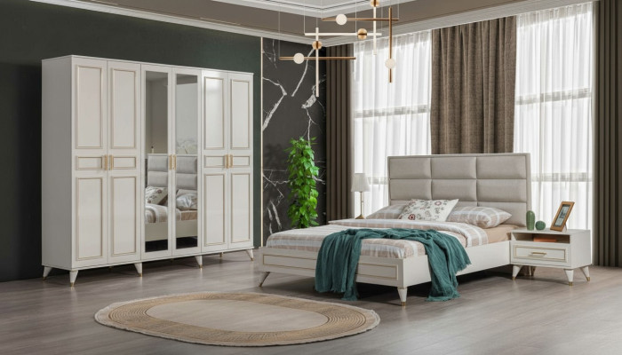 Muebles de dormitorio blancos de madera con armario de vidrio y cama doble de tela con mesitas de noche.