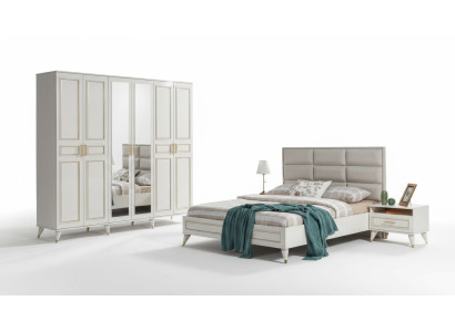 Muebles de dormitorio blancos de madera con armario de vidrio y cama doble de tela con mesitas de noche.